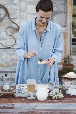 Italien, lachende Frau, die auf einer Terrasse Marmelade auf eine Scheibe Brot schmiert, lizenzfreies Stockfoto