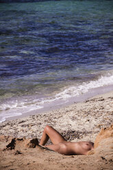 Naked woman sunbathing on the beach at seaside - CMF00744