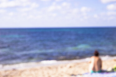 Unscharfe Rückenansicht einer Frau, die am Strand sitzt und die Aussicht betrachtet - CMF00745