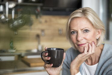 Porträt einer lächelnden älteren Frau mit Kaffeetasse in der Küche - FMKF04625