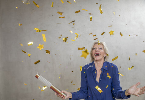 Portrait of amazed senior woman watching golden confetti - FMKF04628