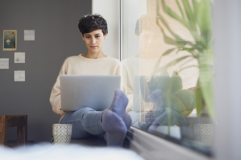 Woman at home sitting at the window using laptop stock photo