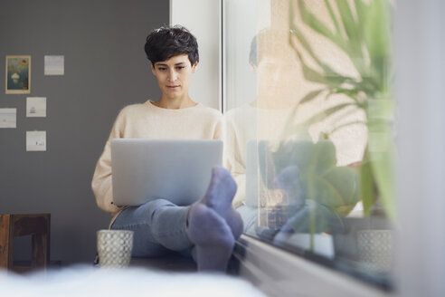 Woman at home sitting at the window using laptop - RBF06101