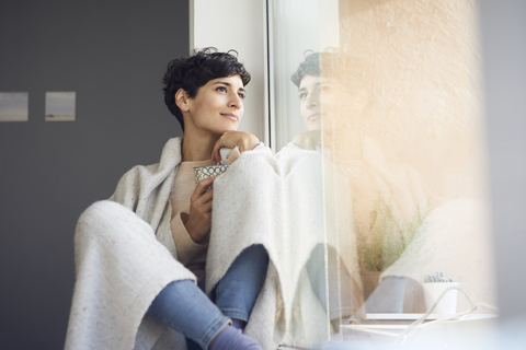Entspannte Frau zu Hause am Fenster sitzend, lizenzfreies Stockfoto
