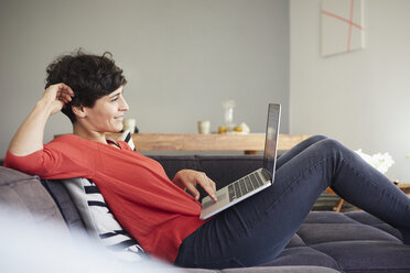 Smiling woman using laptop on couch at home - RBF06130