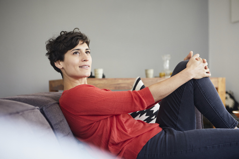Porträt einer lächelnden Frau auf der Couch zu Hause, die nachdenkt, lizenzfreies Stockfoto