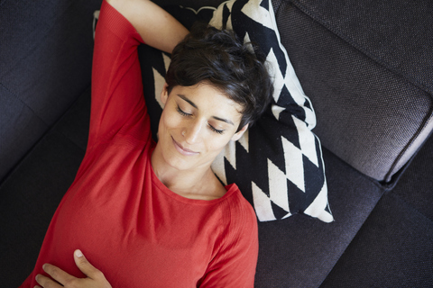 Lächelnde Frau auf der Couch zu Hause mit geschlossenen Augen liegend, lizenzfreies Stockfoto