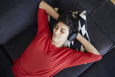 Woman lying on couch at home wearing headphones - RBF06136