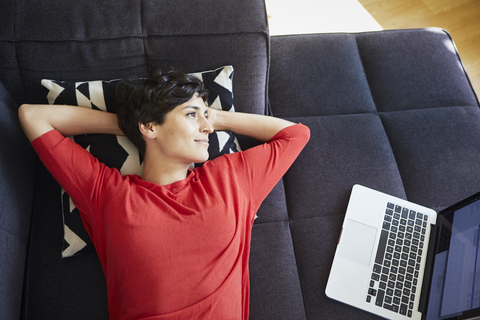 Woman lying on couch at home next to laptop stock photo