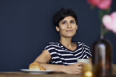 Portrait of smiling woman at home sitting at wooden table - RBF06144