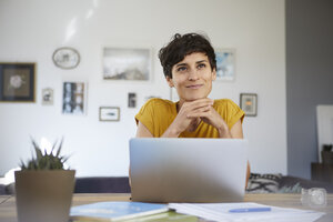 Porträt einer lächelnden Frau, die zu Hause am Tisch sitzt und einen Laptop benutzt - RBF06148