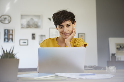 Porträt einer lächelnden Frau, die zu Hause am Tisch sitzt und einen Laptop benutzt - RBF06149