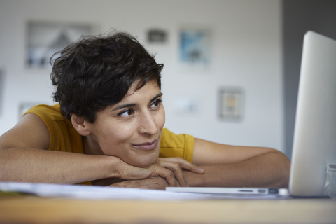 Smiling woman at home leaning on table looking at laptop stock photo