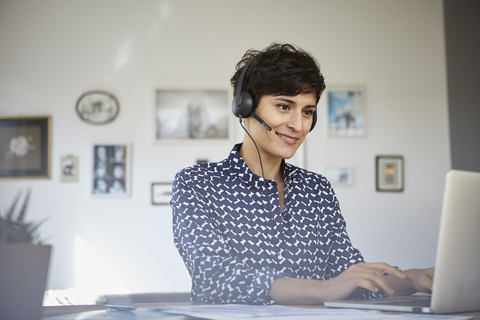 Lächelnde Frau zu Hause mit Headset und Laptop, lizenzfreies Stockfoto