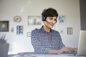 Lächelnde Frau zu Hause mit Headset und Laptop - RBF06154