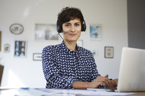 Portrait of smiling woman at home with headset and laptop - RBF06155