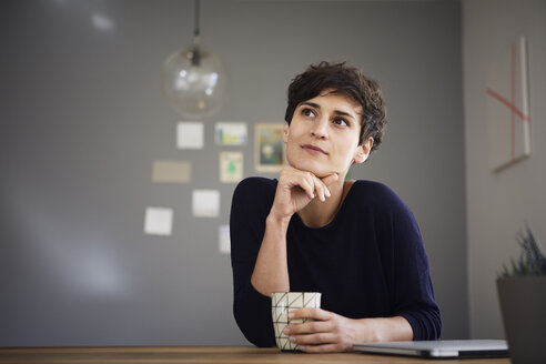 Porträt einer Frau zu Hause am Tisch sitzend mit einer Tasse Kaffee - RBF06157