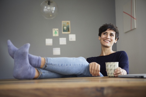 Lächelnde Frau zu Hause am Tisch sitzend mit einer Tasse Kaffee, lizenzfreies Stockfoto