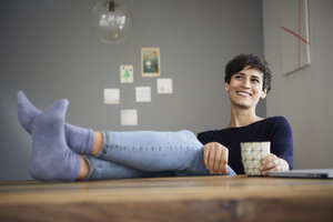 Lächelnde Frau zu Hause am Tisch sitzend mit einer Tasse Kaffee - RBF06159