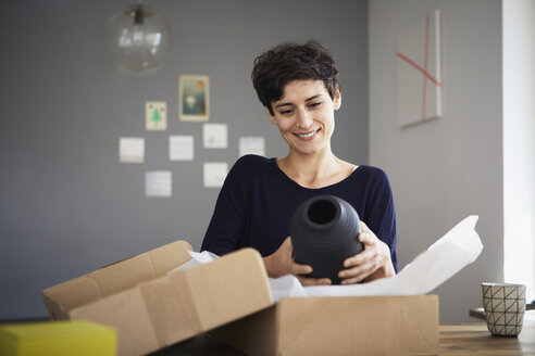 Smiling woman unpacking parcel at home - RBF06162