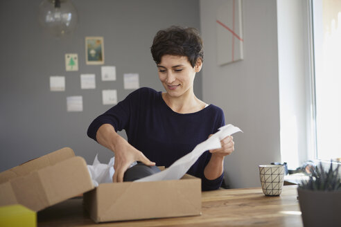 Smiling woman packing parcel at home - RBF06163