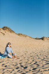 Portugal, Aveiro, Frau sitzt in der Nähe der Stranddüne und hört mit Kopfhörern Musik - JPF00277
