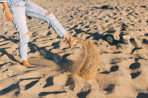 Woman standing on one leg throwing sand on the beach, partial view - JPF00279