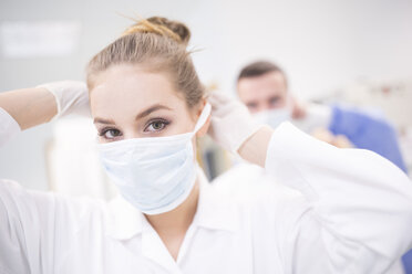 Portrait of lab technician putting on mask - WESTF23629