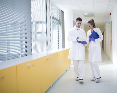 Mann und Frau in Laborkitteln diskutieren auf dem Flur, lizenzfreies Stockfoto