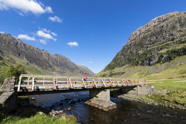 Großbritannien, Schottland, Schottische Highlands, Glencoe, Loch Achtriochtan, weibliche Touristin geht über Brücke - FOF09493