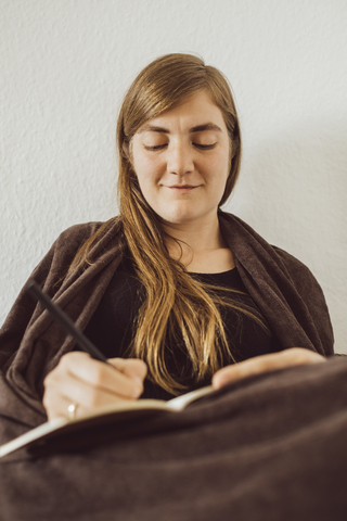 Smiling woman writing in notebook at home stock photo