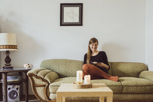 Frau sitzt auf der Couch im Wohnzimmer und schreibt in ein Notizbuch - JSCF00019