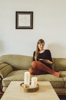 Frau sitzt auf der Couch im Wohnzimmer und schreibt in ein Notizbuch - JSCF00020