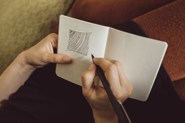 Hand einer Frau auf der Couch, die in ein Notizbuch zeichnet, Nahaufnahme - JSCF00021