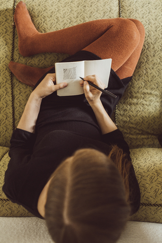 Woman sitting on couch drawing in notebook, top view stock photo