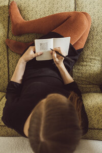 Frau sitzt auf der Couch und zeichnet in ein Notizbuch, Draufsicht - JSCF00022