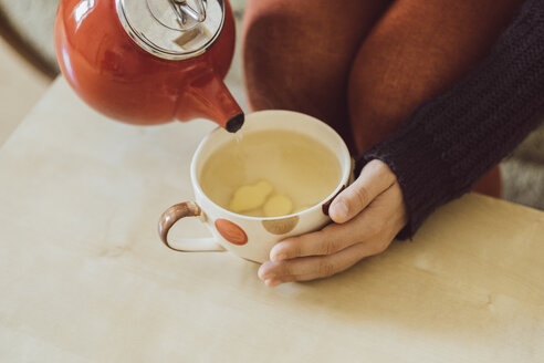 Woman pouring water into tea cup with chopped fresh ginger, close-up - JSCF00023