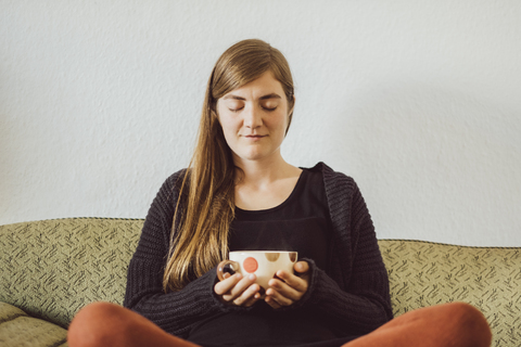 Woman with eyes closed sitting on couch with tea cup stock photo