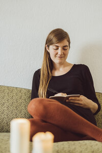 Lächelnde Frau sitzt auf der Couch und schreibt in ein Notizbuch - JSCF00026