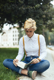 Teenager-Mädchen sitzt im Schneidersitz in einem Park und liest ein Buch - GIOF03311