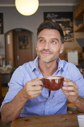 Porträt eines lächelnden Mannes mit einer Tasse Kaffee in einem Kaffeehaus - PNEF00340
