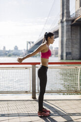 Woman doing stretching exercises in Manhattan near Brooklyn Bridge in the morning - GIOF03338