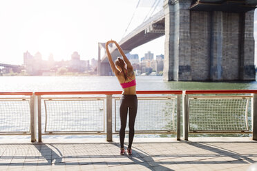 Woman doing stretching exercises in Manhattan near Brooklyn Bridge in the morning - GIOF03339