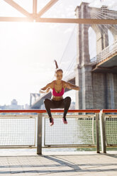 Female athlete training in Manhattan near Brooklyn Bridge, jumping mid air - GIOF03340