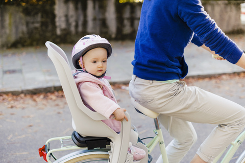 Mother and daughter riding bicycle, baby wearing helmet sitting in children's seat stock photo