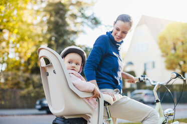 Mother and daughter riding bicycle, baby wearing helmet sitting in children's seat - DIGF03169