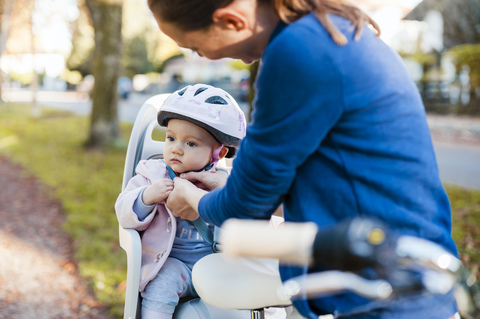 Mother and daughter riding bicycle, baby wearing helmet sitting in children's seat stock photo