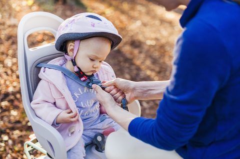 Mutter und Tochter fahren Fahrrad, das Baby trägt einen Helm und sitzt im Kindersitz, lizenzfreies Stockfoto