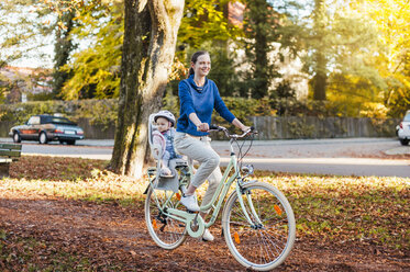 Mother and daughter riding bicycle, baby wearing helmet sitting in children's seat - DIGF03172