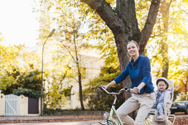 Mutter und Tochter fahren Fahrrad, das Baby trägt einen Helm und sitzt im Kindersitz - DIGF03173